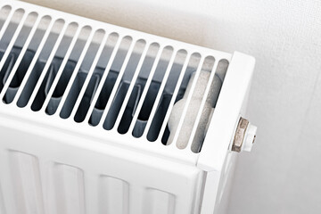 Close-up of an old white radiator with a heating valve and metal pipes, showing signs of wear. A detailed shot illustrating home heating, energy efficiency, and plumbing maintenance