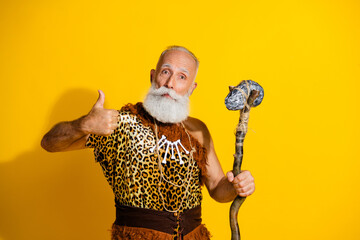Photo of ancient aged caveman hold ax show thumb up wear leopard skin clothes isolated on yellow color background