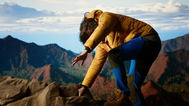 Battling intense wind and searching for better telephone signal, young hiker acting reckless distracted by smartphone on mountain top. Tumbling on the steep cliffs of a scenic peak. Camera B.