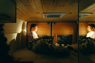 Naklejka premium Young caucasian female child girl relaxing in cozy wooden camper interior with soft lighting and blanket. Spain Square, Plaza de Espana