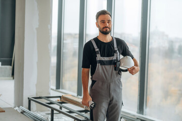 In grey uniform and black shirt. A man is renovating an unfinished room