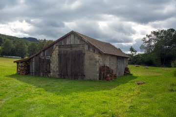 A rustic barn stands in an expansive green field, under a cloudy sky, showcasing a peaceful rural...