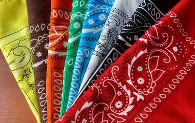 Brightly colored bandanas with intricate paisley designs are neatly displayed in a fan shape on a polished wooden surface. Each bandana features unique colors and patterns, creating a lively visual