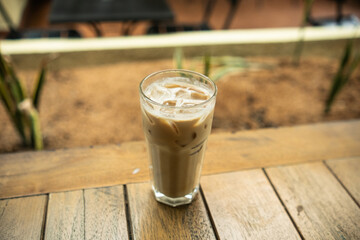 An iced café latte placed on a table with a blurred background of multiple tables in an outdoor setting, creating a relaxed café atmosphere