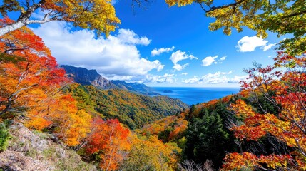Fototapeta premium Vibrant autumn foliage frames a scenic mountain valley overlooking a blue sea under a sunny sky.