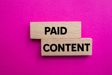 Paid content message written on wooden blocks on pink background. Conceptual paid content symbol. Copy space.