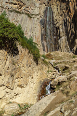 Beautiful Abai-Su waterfall cascades down rugged cliffside, surrounded by lush greenery and rocky terrain, creating picturesque natural scene. Kabardino-Balkaria, Chegemsky district