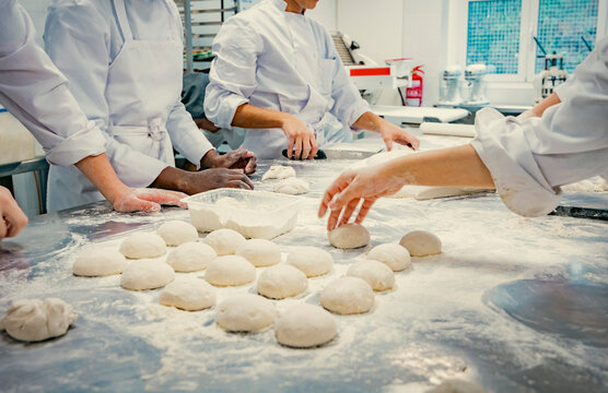 Hands of baking students working with fresh dough in a professional kitchen. Artisan bread preparation, teamwork, and pastry training in a culinary school. Flour, dough balls, and rolling techniques.