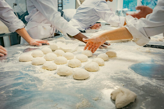 Hands of baking students working with fresh dough in a professional kitchen. Artisan bread preparation, teamwork, and pastry training in a culinary school. Flour, dough balls, and rolling techniques.