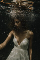 Obraz premium close-up photo of a blonde young woman submerged in water, her delicate face illuminated by rippling sunlight. Her expression is serene, with slightly parted lips and closed eyes, as if lost 