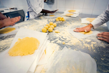 Students in a bakery school flattening dough balls by hand on a floured stainless steel table. Hands-on pastry training in a professional kitchen, learning traditional baking techniques.