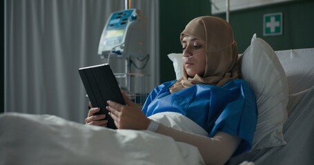 In the hospital ward, the young patient uses a tablet to chat with someone.