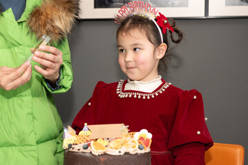 A little multiracial girl is celebrating her fourth birthday in a red formal dress with bows in her...