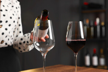 Professional sommelier pouring red wine into glasses at wooden table indoors, closeup