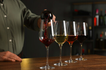 Professional sommelier pouring red wine into glasses on wooden table indoors, closeup
