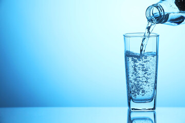 Pouring soda water from bottle into glass on light blue background, closeup. Space for text