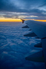 Obraz premium Vertical view from airplane window of aircraft flying above dramatic clouds in colourful sunset sky background. Transportation or travel concept