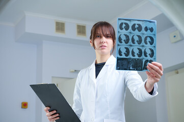 Young female radiologist staying in scanning room holding CT film. Working in the clinic. Pretty...