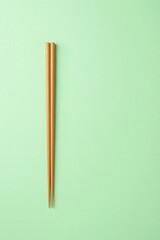 A pair of simple wooden chopsticks rests on a pale green background, a minimalist composition.