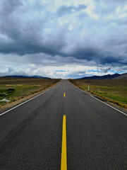 Endless straight road through the Andes mountains under a dramatic sky, Peru.