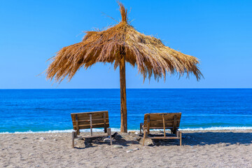 Straw beach umbrella with sun loungers on the sandy beach of the Black Sea in Gagra.Trips, vacation travel. Can be used as an illustration and background in articles about traveling in Abkhazia.