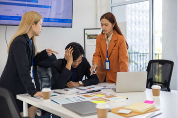 Three people are in a meeting room, with one of them pointing at a laptop screen. The man on the laptop is looking down, and the other two people are looking at him. Scene is tense and serious
