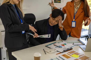 Three people are in a meeting room, with one of them pointing at a laptop screen. The man on the laptop is looking down, and the other two people are looking at him. Scene is tense and serious
