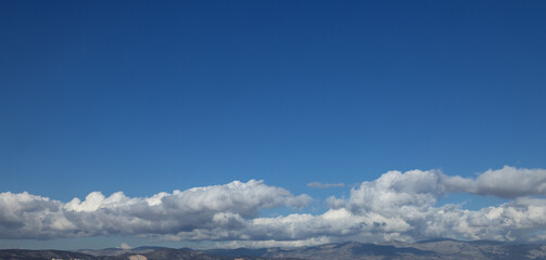 Obraz premium Band of white cumulus clouds is low over the hilly horizon of the blue sky