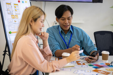 Obraz premium Three people are sitting around a table, working on a project. They are wearing name tags and are pointing at a whiteboard. Scene is collaborative and focused 