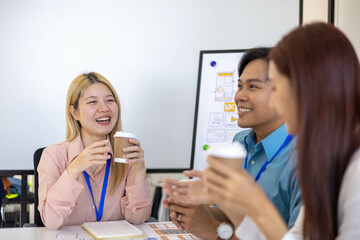 Three people are sitting around a table, working on a project. They are wearing name tags and are pointing at a whiteboard. Scene is collaborative and focused
