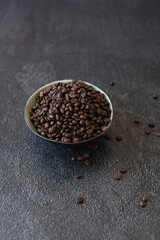 Pile of coffee beans in a bowl spilling over the side on a dark and moody background. 