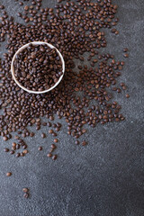 Pile of coffee beans in a bowl spilling over the side on a dark and moody background.  Overhead top shot, textured wallpaper background
