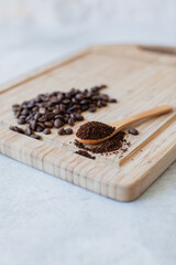 Ground coffee on a spoon next to a pile of coffee beans on a wooden board
