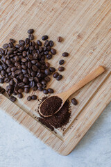 Ground coffee on a spoon next to a pile of coffee beans on a wooden board