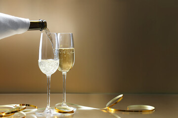 Pouring champagne into glass against golden background, closeup. Space for text