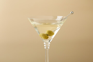 Martini cocktail with olives in glass on beige background, closeup