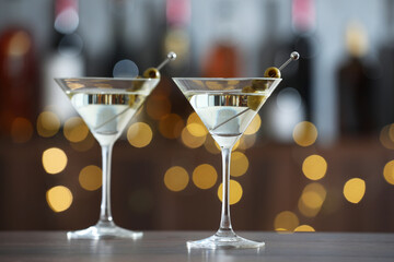 Martini cocktail with olives in glasses on wooden table against blurred background. Bokeh effect