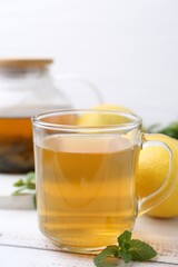 Aromatic mint tea with lemons and fresh leaves on white wooden table, closeup