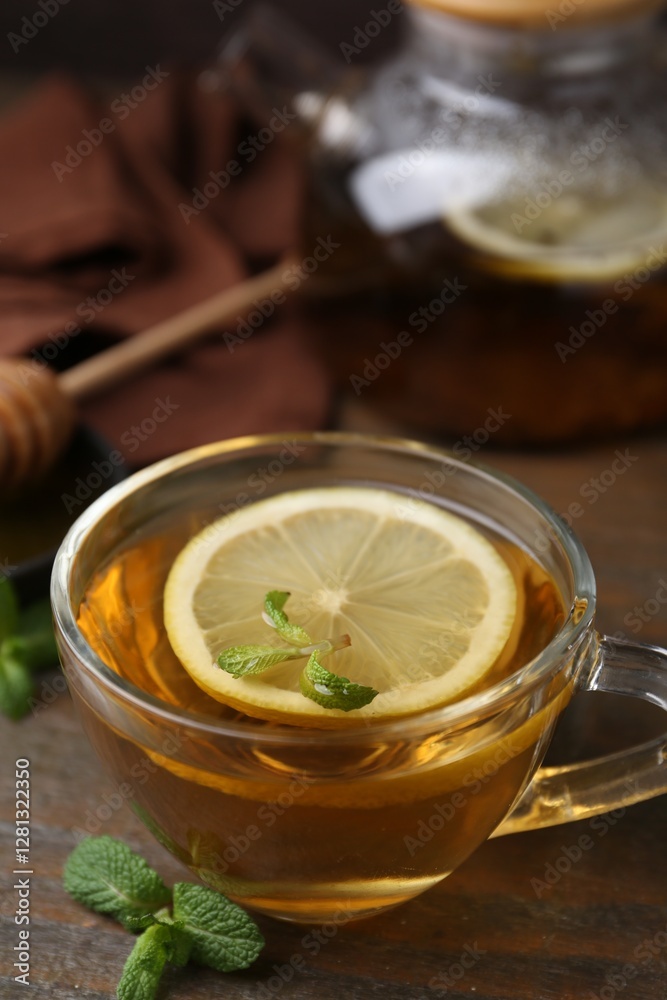 Sticker Tasty mint tea in cup, lemon and fresh leaves on wooden table, closeup