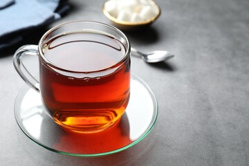 Refreshing black tea in cup on grey textured table, closeup. Space for text