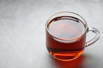 Refreshing black tea in cup on grey table, closeup. Space for text