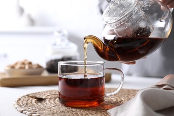 Woman pouring hot black tea into cup at white table, closeup