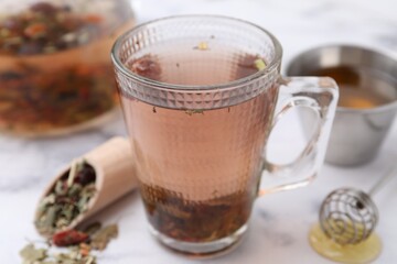 Delicious herbal tea with honey and dry leaves on white marble table, closeup