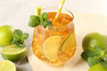 Refreshing iced tea with slices of lime, mint and drinking straw in glass on light table, closeup