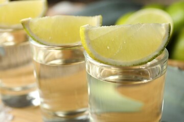 Tequila shots with lime slices on table, closeup