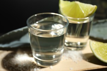 Tequila shots, slices of lime, salt and agave leaves on table against black background, closeup