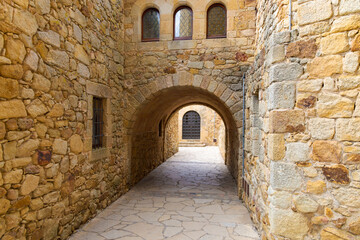 Calle medieval empedrada con arco de piedra y ventanas de vidrio en Pals, Cataluña, España.