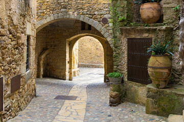 Portal de acceso al Padro con arcos de piedra, calle empedrada y macetas en Pals, Catalu&ntilde;a, Espa&ntilde;a.