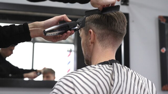Professional barber trimming male client's hair using electric razor, creating precise haircut in contemporary barbershop setting with sleek styling tools