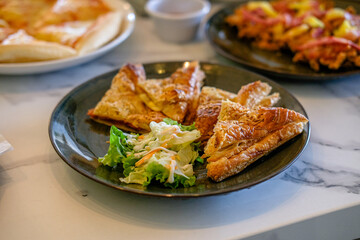 Pastry cookies, cheese pie, sliced ​​tomatoes, carrots and green vegetables on a black ceramic plate